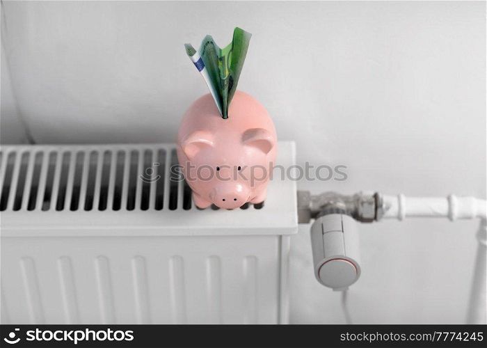 heating, energy crisis and consumption concept - piggy bank with money on radiator at home. piggy bank with money on radiator at home