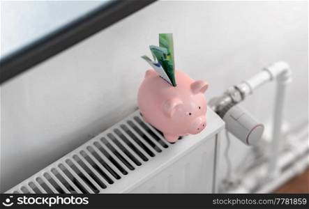 heating, energy crisis and consumption concept - piggy bank with money on radiator at home. piggy bank with money on radiator at home