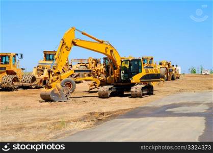 Heavy construction equipment sits idle lined up along a new asphalt road. Excavator And Heavy Equipment