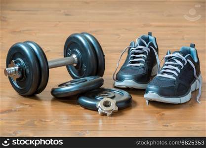 Heavy dumbbell and black men's sneakers on the wooden floor
