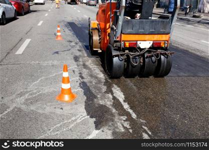 Heavy orange vibrating roller compacts hot asphalt renews a part of the road of the city street, image with copy space.. Heavy orange vibratory road roller compacts asphalt on the repaired part of the citys road.