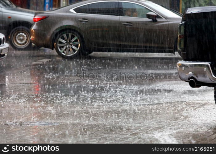 Heavy rain falls on passing cars on a city road. Blurred rain background. ?opy space.. Large drops of heavy rain on a city road.