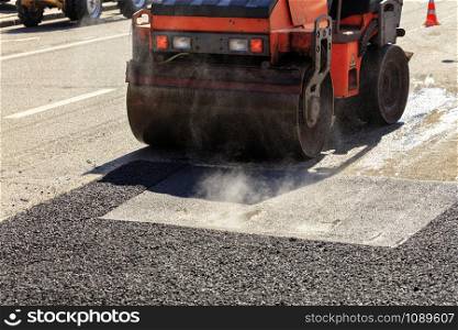 Heavy vibrating roller compacts hot asphalt on the repaired asphalt surface of the carriageway on a clear sunny day. A heavy vibratory road roller compacts asphalt on the road to be repaired.