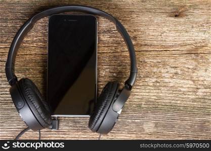 Hedphones with phone. Black headphones with modern phone on wooden background