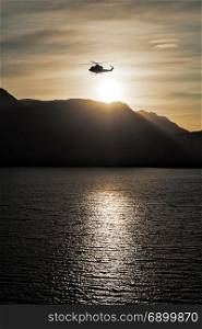 Helicopter flying over the sea at sunset with mountains on background. Helicopter flying over the sea at sunset