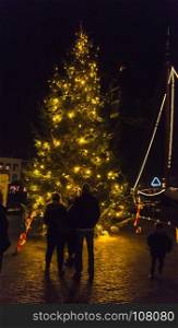 HELLEVOETSLUIS,HOLLAND,15-12-2017: Unidentified people at the christmas tree at night , the christmas tree is illuminated one week for christmas. people at the christmas tree