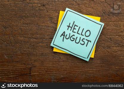 Hello August - handwriting on a sticky note against rustic wood