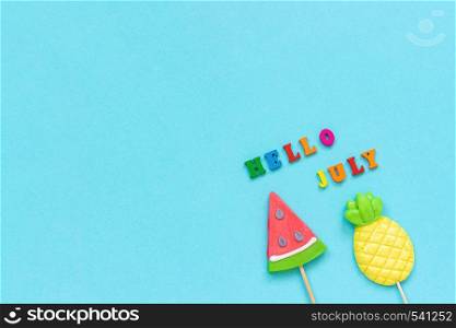 Hello July colorful text, pineapple and watermelon lollipops on stick on blue paper background. Concept vacation or holidays Creative Top view Copy space Template Greeting card, postcard.. Hello July colorful text, pineapple and watermelon lollipops on stick on blue paper background. Concept vacation or holidays Creative Top view Copy space Template Greeting card, postcard