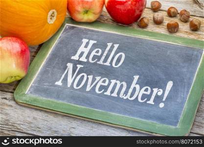 Hello November on a slate blackboard with apples, pumpkin and hazelnuts against grunge barn wood