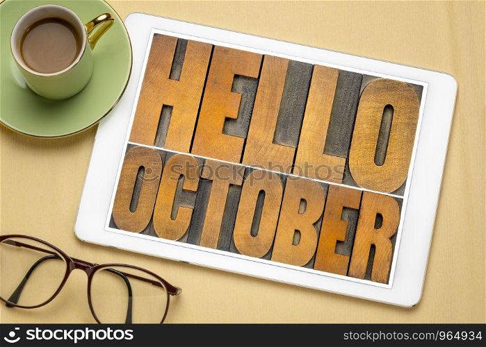 Hello October - word abstract in vintage letterpress wood type blocks on a screen of a digital tablet, flat lay with coffee and glasses