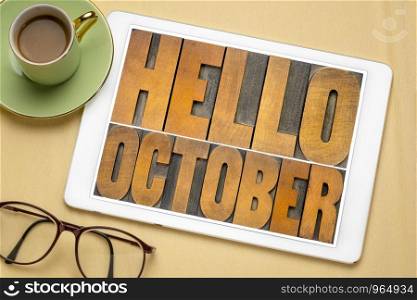 Hello October - word abstract in vintage letterpress wood type blocks on a screen of a digital tablet, flat lay with coffee and glasses