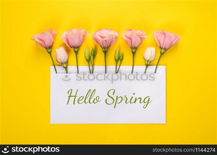 Hello spring banner. Pink Eustoma flowers arrangement with blank card on yellow background. Copy space. Top view. Hello spring banner. Pink Eustoma flowers arrangement with blank card on yellow background