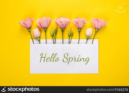 Hello spring banner. Pink Eustoma flowers arrangement with blank card on yellow background. Copy space. Top view. Hello spring banner. Pink Eustoma flowers arrangement with blank card on yellow background