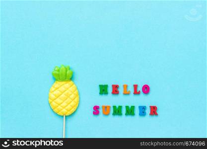 Hello summer text from colorful letters, pineapple lollipop on stick on blue paper background. Concept vacation or holidays Creative Top view Copy space Template Greeting card, postcard.. Hello summer text from colorful letters, pineapple lollipop on stick on blue paper background. Concept vacation or holidays Creative Top view Copy space Template Greeting card, postcard