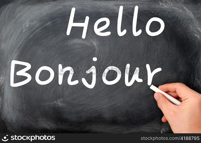 Hello with French Bonjour written on a blackboard background with a hand holding chalk