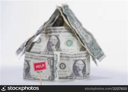 Help sign board in front of a miniature house made by US dollar bills