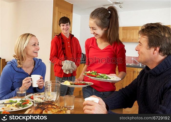Helpful Teenage Children Serving Food To Parents In Kitchen
