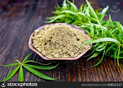 Hemp flour in a bowl, green cannabis leaves on the background of dark wooden boards