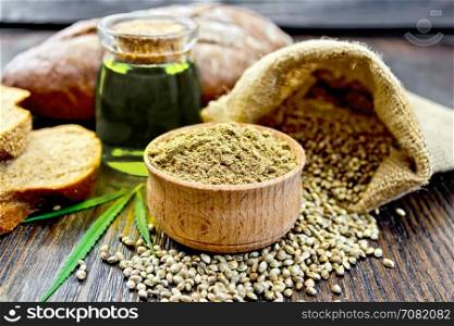 Hemp flour in a bowl, seed in a bag on the table, oil in a glass jar, cannabis leaf and bread on a wooden boards background
