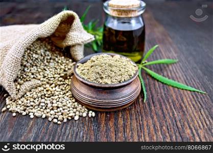 Hemp flour in a clay bowl, the grain in the bag and on the table, the oil in a glass jar, leaves and stalks of cannabis on a background of wooden boards