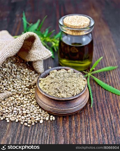 Hemp flour in a clay bowl, the grain in the bag and on the table, the oil in a glass jar, cannabis leaves on the background of wood planks