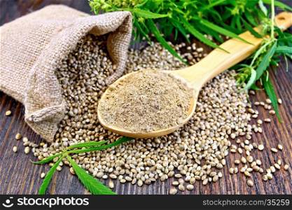 Hemp flour in a spoon, the grain in the bag and on the table, leaves and stalks of cannabis on the background of dark wood planks
