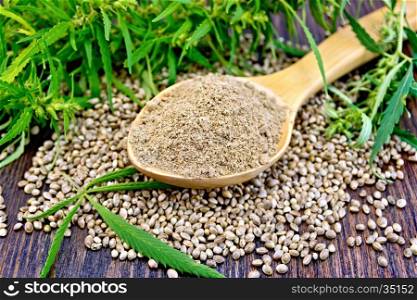 Hemp flour in a wooden spoon, the grain on the table, leaves and stalks of cannabis on the background of dark wood planks