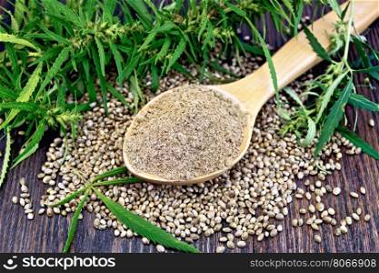 Hemp flour in a wooden spoon, the grain on the table, leaves and stalks of cannabis on the background of wood planks