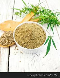 Hemp flour in white bowl, grain in spoon, cannabis leaves on the background of the wooden boards