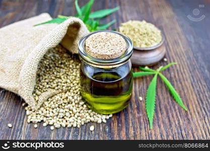 Hemp oil in a glass jar with flour in a clay bowl and grain in a bag, cannabis leaves and stalks on a wooden boards background