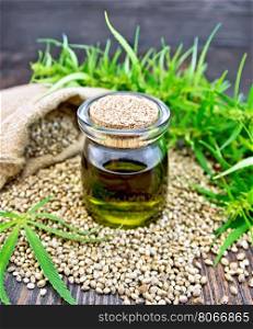 Hemp oil in a glass jar with grain in a bag, cannabis leaves and stalks on a wooden boards background