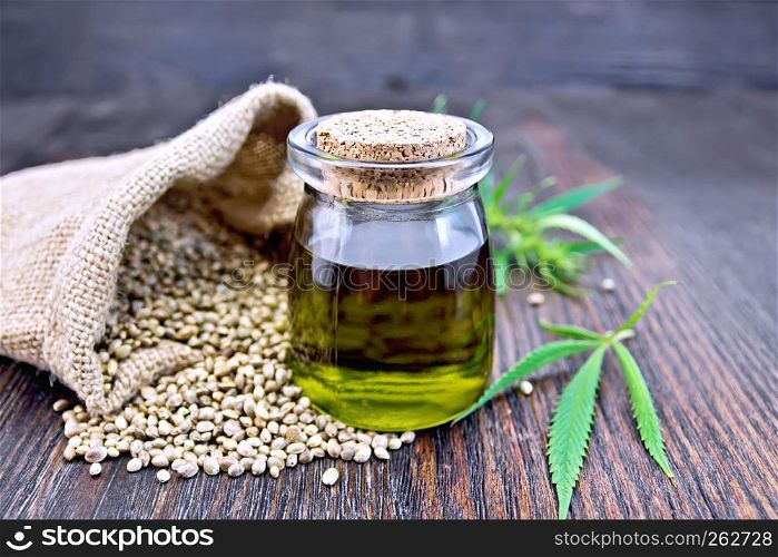 Hemp oil in a glass jar with grain in a bag, leaves and stalks of cannabis on the background of a dark wooden board
