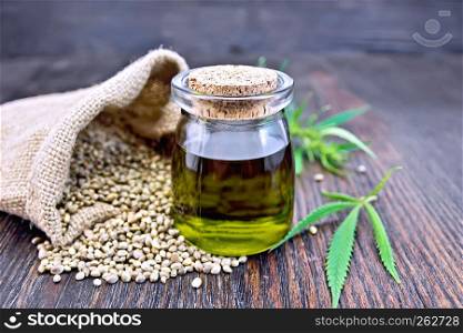 Hemp oil in a glass jar with grain in a bag, leaves and stalks of cannabis on the background of a dark wooden board