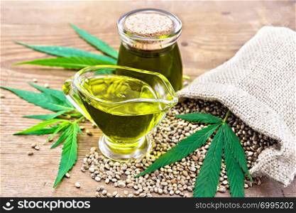 Hemp oil in a glass sauceboat and a jar with grain in a bag, leaves and stalks of cannabis on a wooden board background