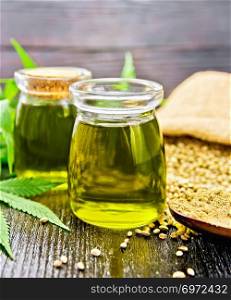 Hemp oil in two glass jars, grain in a bag and on the table, flour in a spoon, cannabis
 leaves on a wooden board background