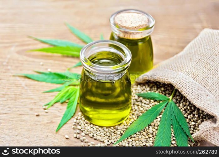 Hemp oil in two glass jars, grain in the bag and on the table, cannabis leaves on the background of an old wooden board