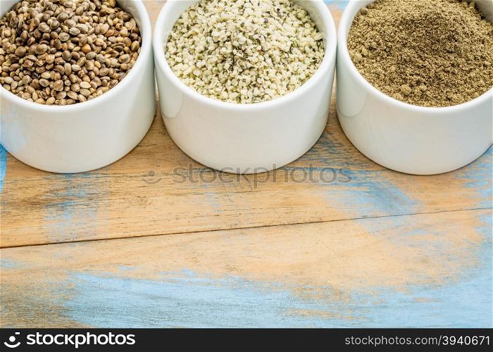 hemp products: seeds, hearts (shelled seeds) and protein powder in small ceramic bowls on a grunge wood with a copy space