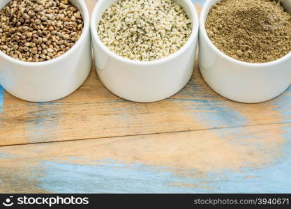 hemp products: seeds, hearts (shelled seeds) and protein powder in small ceramic bowls on a grunge wood with a copy space