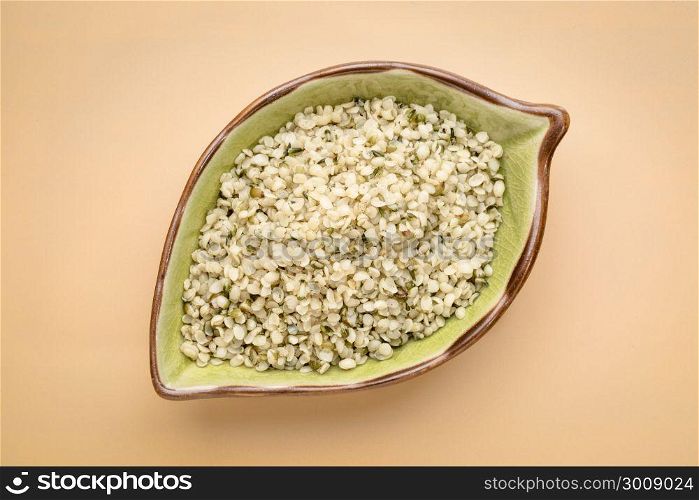 hemp seed hearts on a leaf shaped ceramic bowl, top view against beige background