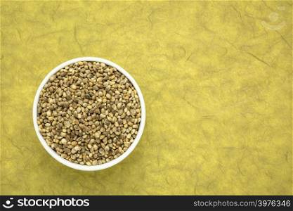 hemp seed in a small ceramic bowl, top view against mulberry paper background