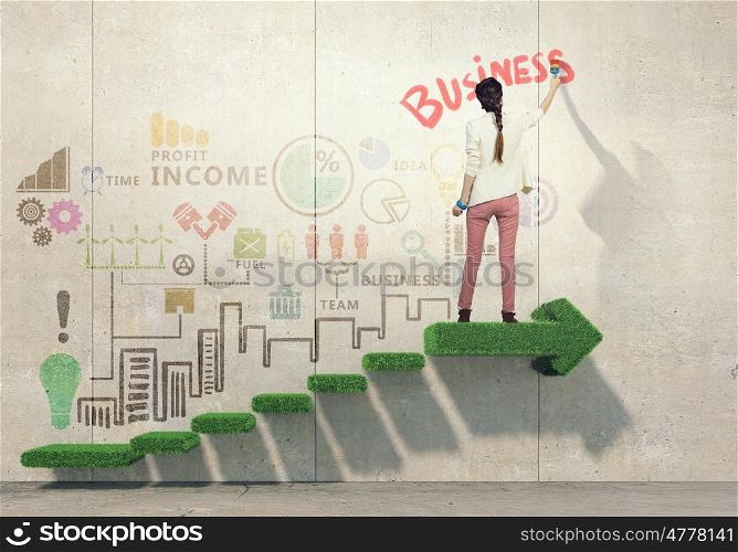Her creative approach to business. Young attractive woman painting business sketches on wall