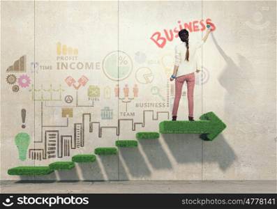Her creative approach to business. Young attractive woman painting business sketches on wall