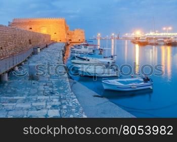 Heraklion. The old Venetian fortress at night.. View of the medieval Venetian Castle and Heraklion port at sunset. Crete. Greece. Boats blurred motion on the foreground.