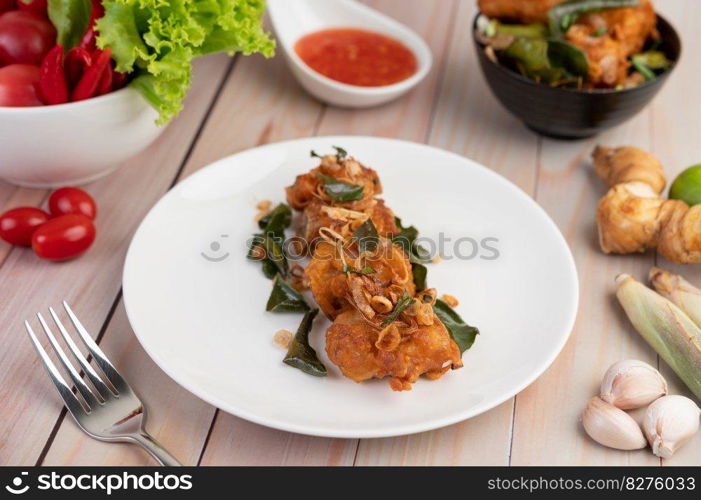 Herb fried chicken on a white plate and dipping sauce with lemongrass, garlic, lemon and tomatoes on a wooden floor