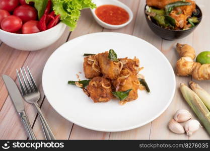 Herb fried chicken on a white plate and dipping sauce with lemongrass, garlic, lemon and tomatoes on a wooden floor