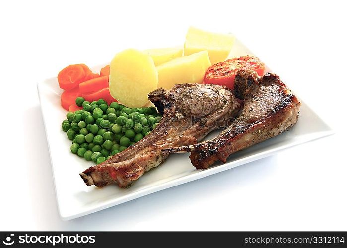 Herb marinaded grilled lamb chops served with boiled potatoes, sliced carrots and peas on a white plate, with a shadow.