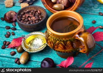 Herbal Autumn Tea. Cup with hot autumnal tea, on background of autumn foliage, cones and nuts