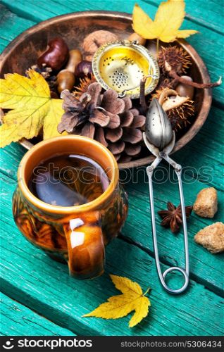 Herbal Autumn Tea. Cup with tea, against the background of autumn foliage, cones and nuts