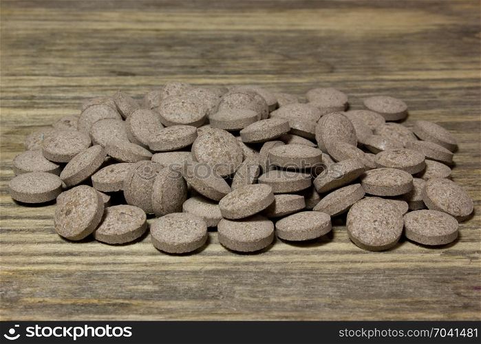Herbal brown pills on wooden background.