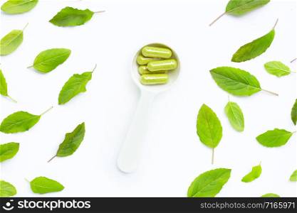 Herbal capsules with fresh holy basil leaves on white background.